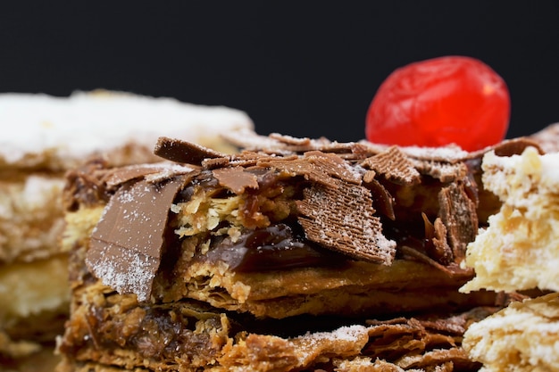 Torte di pasta sfoglia con zucchero a velo e panna e un altro con cioccolato e una ciliegina sulla tavola di legno. Avvicinamento. Messa a fuoco selettiva.