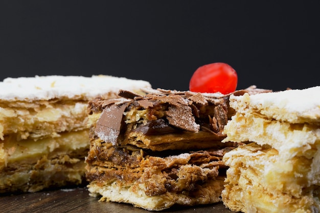 Torte di pasta sfoglia con zucchero a velo e panna e un altro con cioccolato e una ciliegina sulla tavola di legno. Avvicinamento. Messa a fuoco selettiva.