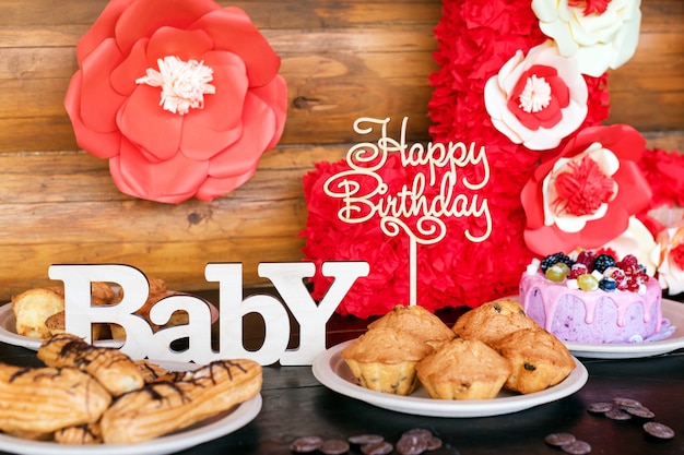 Torte e muffin di compleanno con i segni di saluto di legno sulla parete rustica. Canto in legno con lettere Buon compleanno, Baby e dolci natalizi.