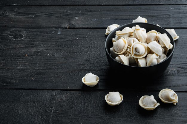 Tortellini congelati in una ciotola nera, su sfondo di tavolo in legno nero, con copyspace e spazio per il testo