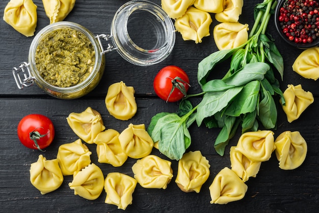 Tortellini crudi con basilico e pesto di pino, sul tavolo di legno nero, vista dall'alto laici piatta