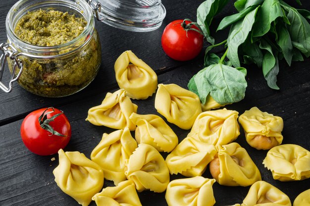 Tortellini crudi con basilico e pesto di pino, sulla tavola di legno nera