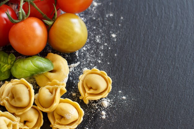 Tortellini italiani crudi fatti in casa con pomodori freschi e basilico su una superficie scura