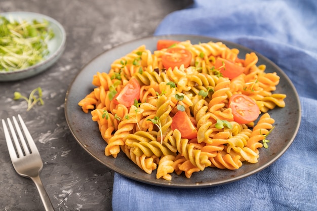 Tortiglioni di pasta di semola con pomodoro e germogli microgreen su una superficie di cemento nero e tessuto blu