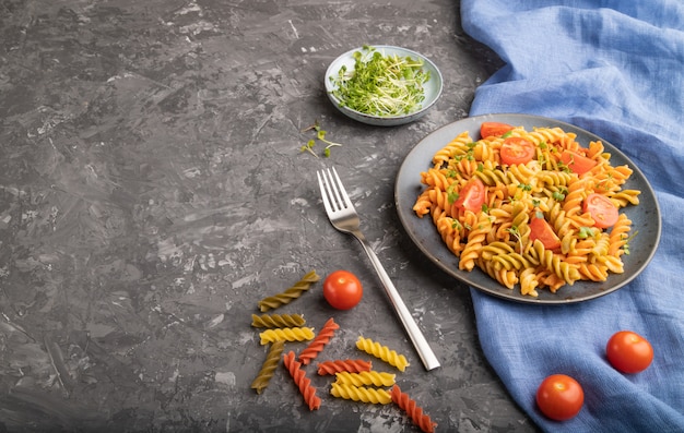 Tortiglioni di semola con pomodoro e germogli di microgreen su fondo nero di cemento. Vista laterale,