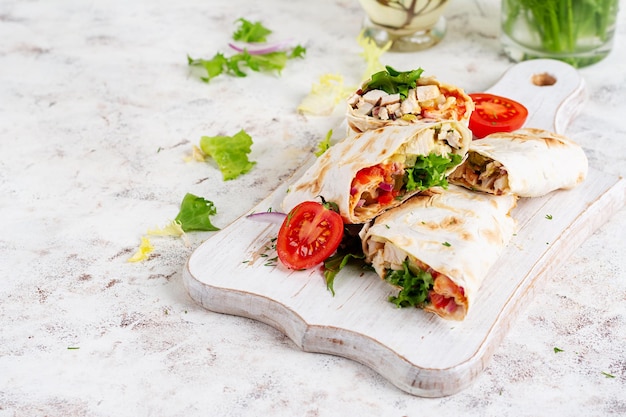 Tortilla alla griglia avvolta con pollo e verdure fresche su tavola di legno bianca Burrito di pollo Cibo messicano Concept alimentare sano