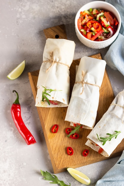 Tortilla avvolge panini con verdure su tavola di legno con insalata, lime e peperoncino