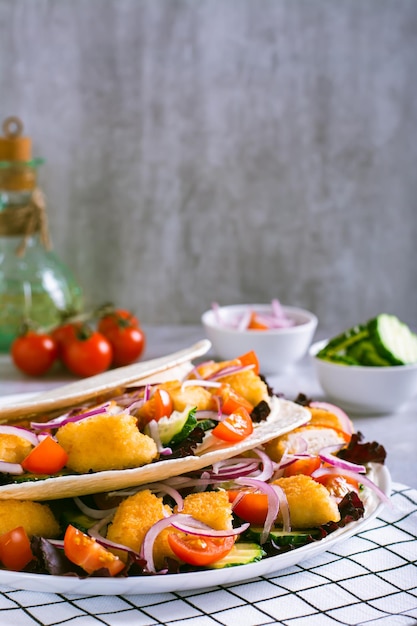 Tortilla con nuggets di pollo, verdure, cipolle e lattuga su un piatto, vista verticale