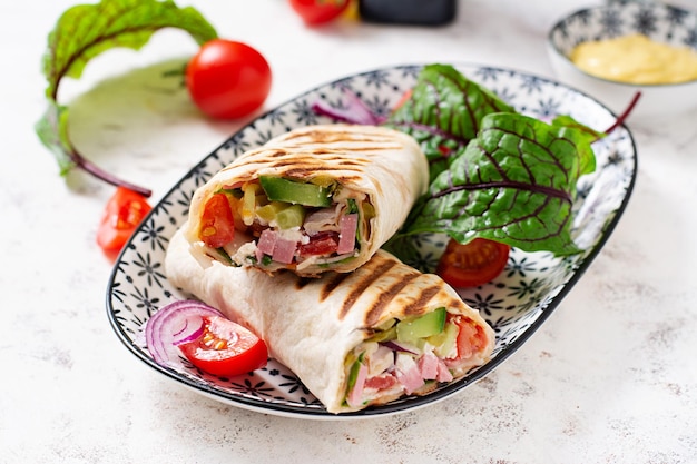 Tortilla wrap con prosciutto, formaggio e pomodori su sfondo bianco Shawarma