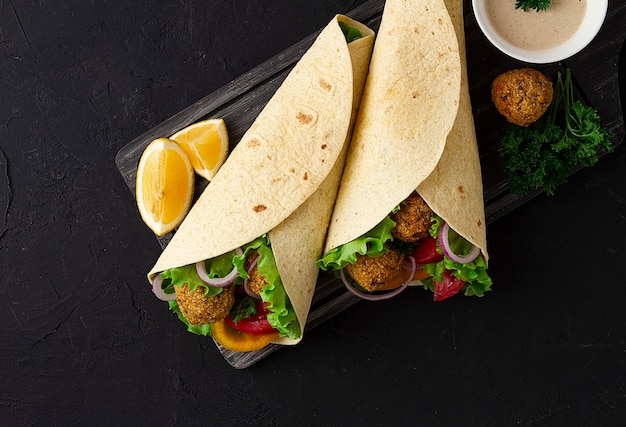 Tortillas avvolte con palline di falafel e verdure fresche cibo sano vegetariano su un nero