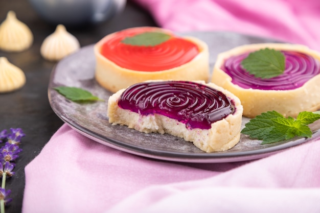 Tortine dolci con gelatina e crema di latte con tazza di caffè su una superficie di cemento nero e tessuto rosa