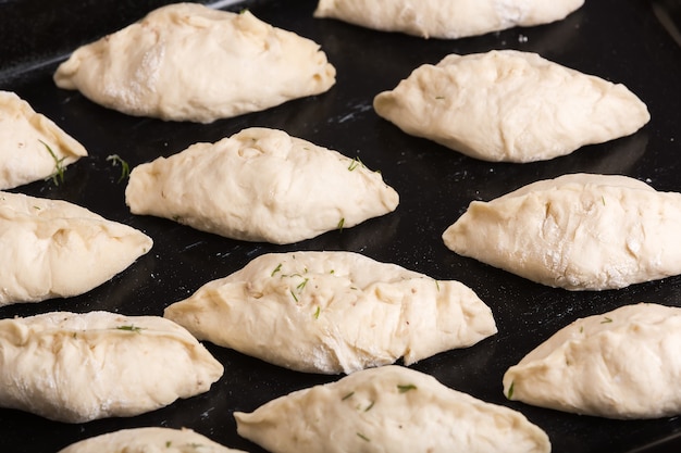 Tortini crudi adagiati su una teglia da forno in acciaio nero e pronti per la cottura. Vista ravvicinata