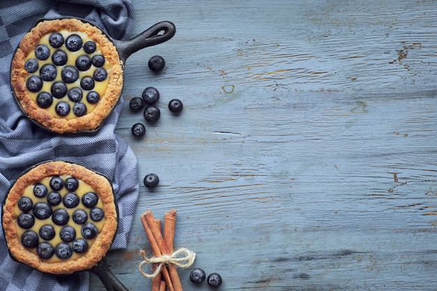 Tortini deliziosi del mirtillo con crema pasticcera alla vaniglia su legno rustico leggero