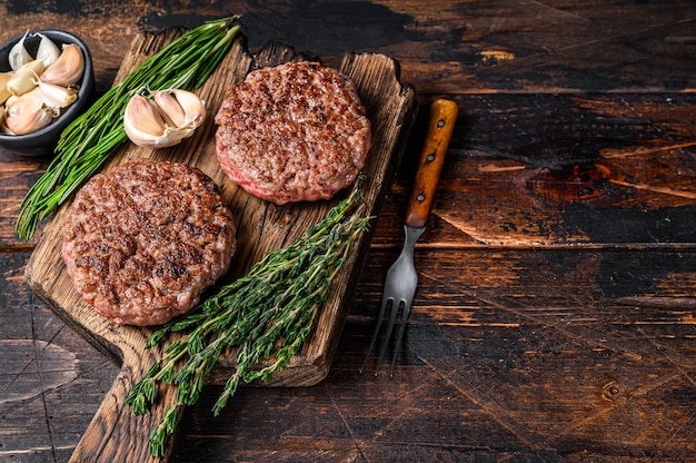 Tortini di bistecca barbecue per hamburger di carne di manzo macinata su un tagliere di legno. Fondo in legno scuro. Vista dall'alto. Copia spazio.