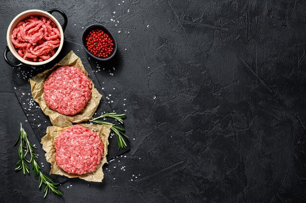 Tortini di carne cruda macinata. Polpette di carne pronte da cuocere. Barbecue. Fattoria biologica di carne. Sfondo nero. Vista dall'alto. Spazio per il testo