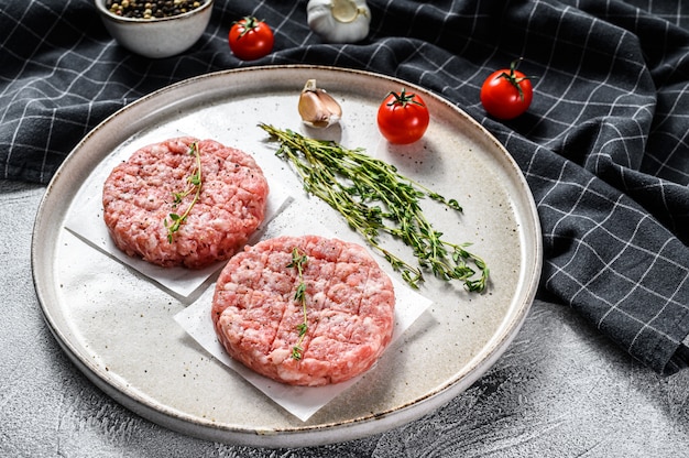 Tortino di maiale crudo, cotolette di carne macinata su un tagliere. Trito Biologico. Sfondo grigio. Vista dall'alto