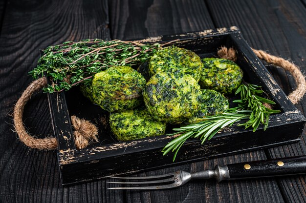 Tortino vegetariano vegetariano di falafel di verdure con erbe in un vassoio di legno. Sfondo nero. Vista dall'alto.