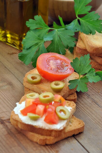 Tostare con pomodoro, olio, olive verdi sul tavolo di legno