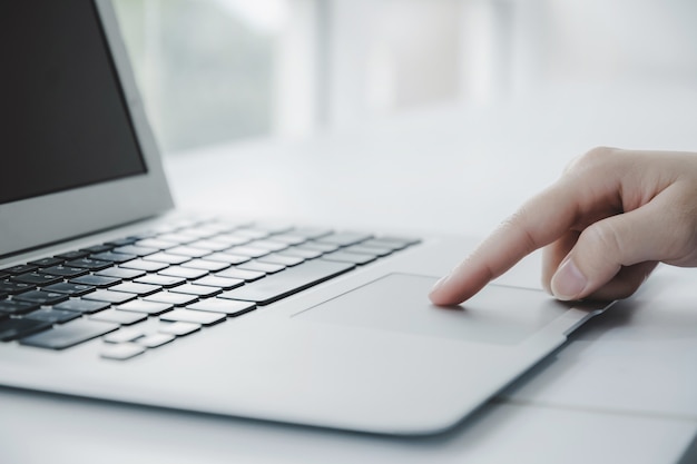 Touchpad commovente della mano del primo piano sul computer portatile sulla scrivania in ufficio a casa, lavoro da casa, ricerca sul web, social network, online, strategia aziendale, finanza, investimento e concetto di tecnologia digitale