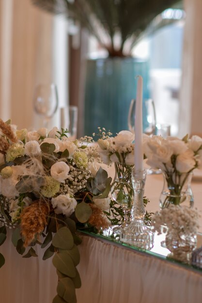 Tovaglie bianche con vasi trasparenti e fiori bianchi e composizioni di felci. Piatti color oro, tovaglioli peavh, numeri da tavola e centrotavola a specchio.