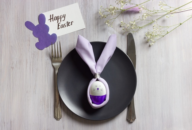 Tovagliolo Easter Bunny sul piatto scuro sul tavolo in legno bianco con carta Buona Pasqua decorata con fiori