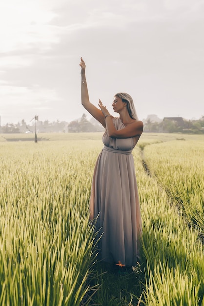 Tra i cespugli del campo di riso si trova in un lungo abito nello stile dell'Impero in posa sotto forma della dea greca donna bionda