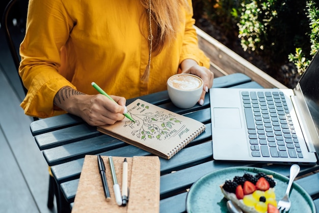 Tracker dell'umore della salute mentale donna seduta in un caffè di strada e riempie il tracker dell'umore nel blocco note