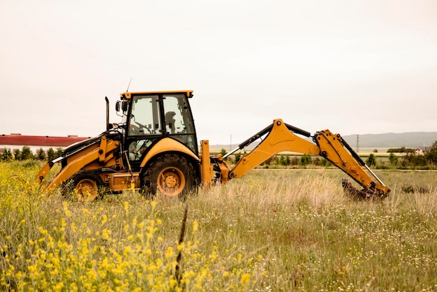 Tractor escavatore sullo sfondo dei fiori primaverili nel campo Preparare i campi per la semina