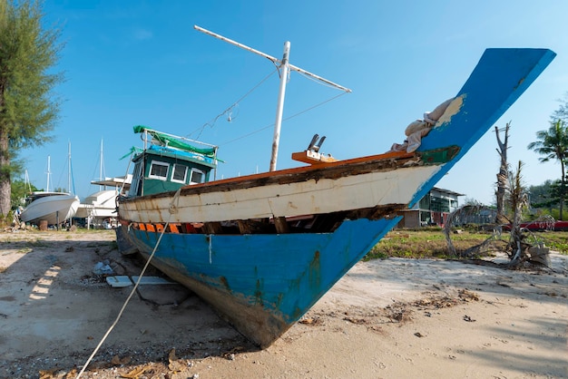 Tradizionale barca da pesca a coda lunga che necessita di riparazione ormeggiata nella sabbia su una spiaggia a Phuket Thailandia