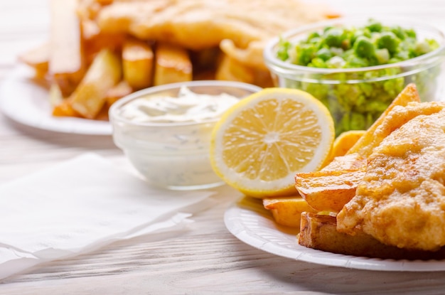 Tradizionale cibo di strada britannico fish and chips con salsa tartara e piselli molli sul piatto di carta