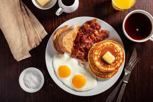 Tradizionale colazione americana completa frittelle di uova con pancetta e pane tostato