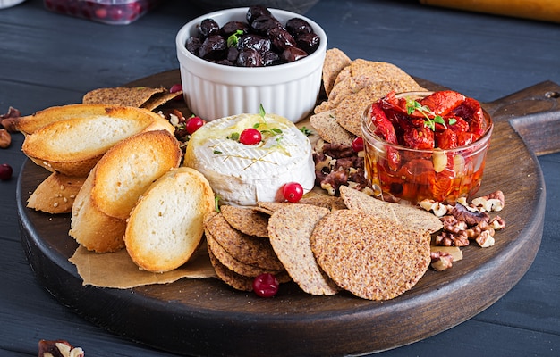 Tradizionale formaggio camembert al forno francese con timo e pane tostato, noci, olive, pomodori secchi e chips di lino.