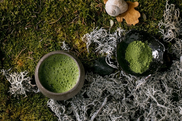 Tradizionale giapponese caldo verde schiumoso tè matcha in tazza di ceramica e matcha in polvere su muschio di foresta come sfondo. Bevanda naturale sana. Vista dall'alto