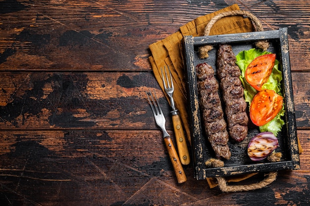 Tradizionale kefta mediorientale o kofta kebab carne macinata di manzo e carne di agnello alla griglia su spiedini serviti con insalata di pomodori e cipolla Fondo in legno Vista dall'alto Copia spazio