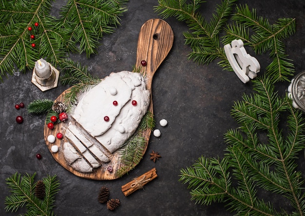 Tradizionale Natale torta di frutta stollen sul tagliere di legno in legno nero rustico sfondo con decorazioni di Natale vista dall'alto con copyspace