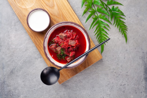 Tradizionale piatto ucraino e russo borsch, zuppa rossa con barbabietole, manzo, panna acida, cucchiaio sulla tavola di legno sul tavolo grigio, close-up, parte superiore