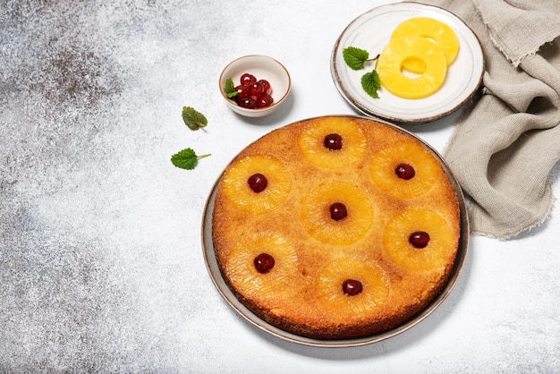 Tradizionale torta rovesciata all'ananas appena sfornata con ciliegie glassate su uno sfondo rustico chiaro