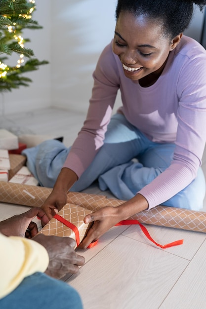 Tradizione natalizia in famiglia giovane coppia africana felice che impara insieme come incartare i regali delle vacanze