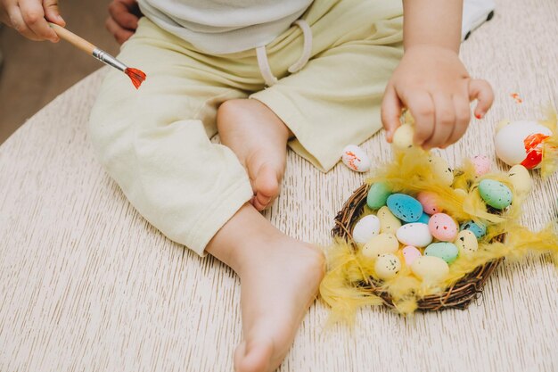 Tradizioni familiari di Pasqua Giovane madre amorevole che insegna ai bambini come dipingere le uova per Pasqua seduti insieme al tavolo della cucina