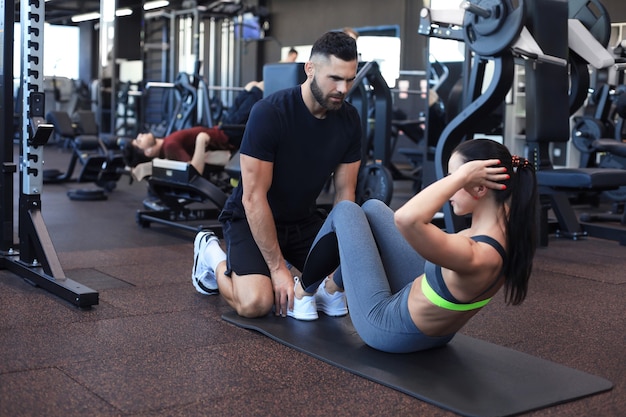 Trainer che aiuta la giovane donna a fare esercizi addominali in palestra.