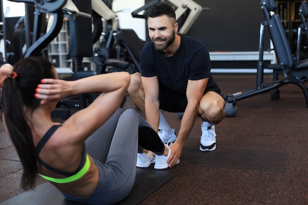 Trainer che aiuta la giovane donna a fare esercizi addominali in palestra.