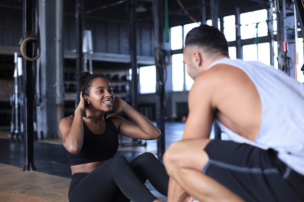 Trainer che aiuta la giovane donna a fare esercizi addominali in palestra.