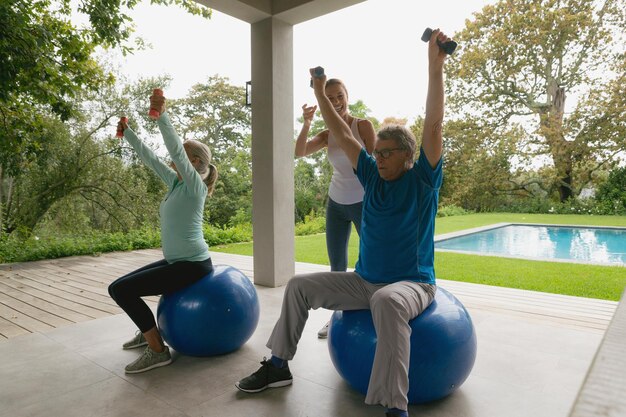 Trainer femminile che aiuta una coppia di anziani attivi ad esercitarsi con un manubrio sul portico