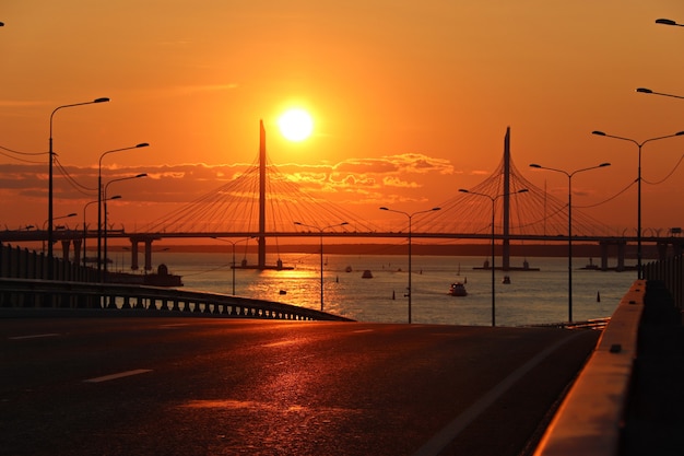 Tramonto arancione sull'autostrada con un grande ponte sul fiume e