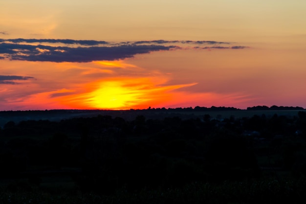 Tramonto arancione sulle sagome del villaggio e degli alberi