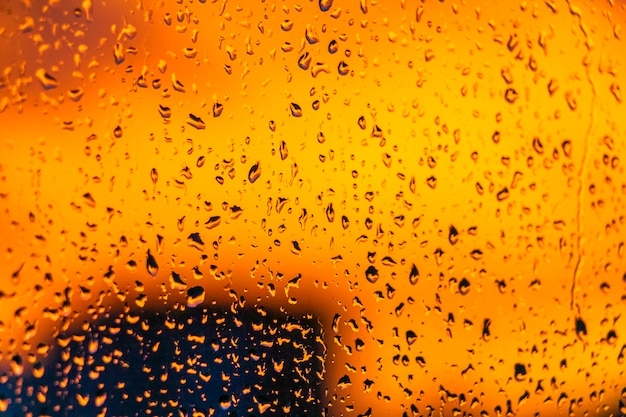 Tramonto ardente luminoso attraverso le gocce di pioggia sulla finestra con l'estratto del bokeh