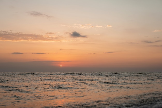 Tramonto colorato su una spiaggia di sabbia, onde con schiuma sulla sabbia. Oceano, costa.