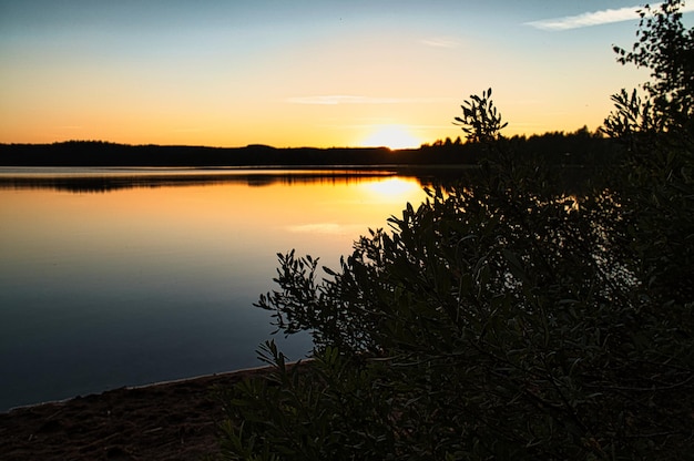 Tramonto con riflesso su un lago svedese a Smalland con cespugli in primo piano