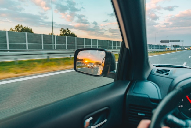 Tramonto dal punto di vista in prima persona nello specchietto retrovisore dell'auto