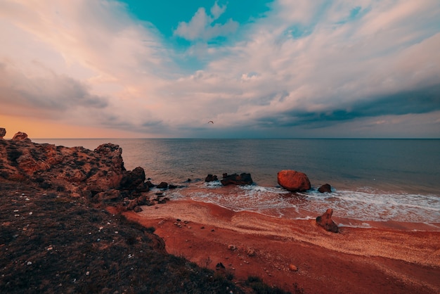 Tramonto in mare. Vista panoramica del mare, costa rocciosa e spiaggia sabbiosa, cielo dorato e sole, sfondo di viaggio all'aperto. Le spiagge del generale. Crimea.